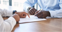 Close-up of a few people signing a document